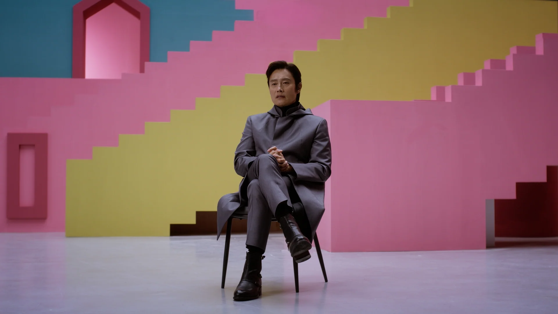 Inside Squid Game S2 — the Front Man actor seated on the pink staircase set