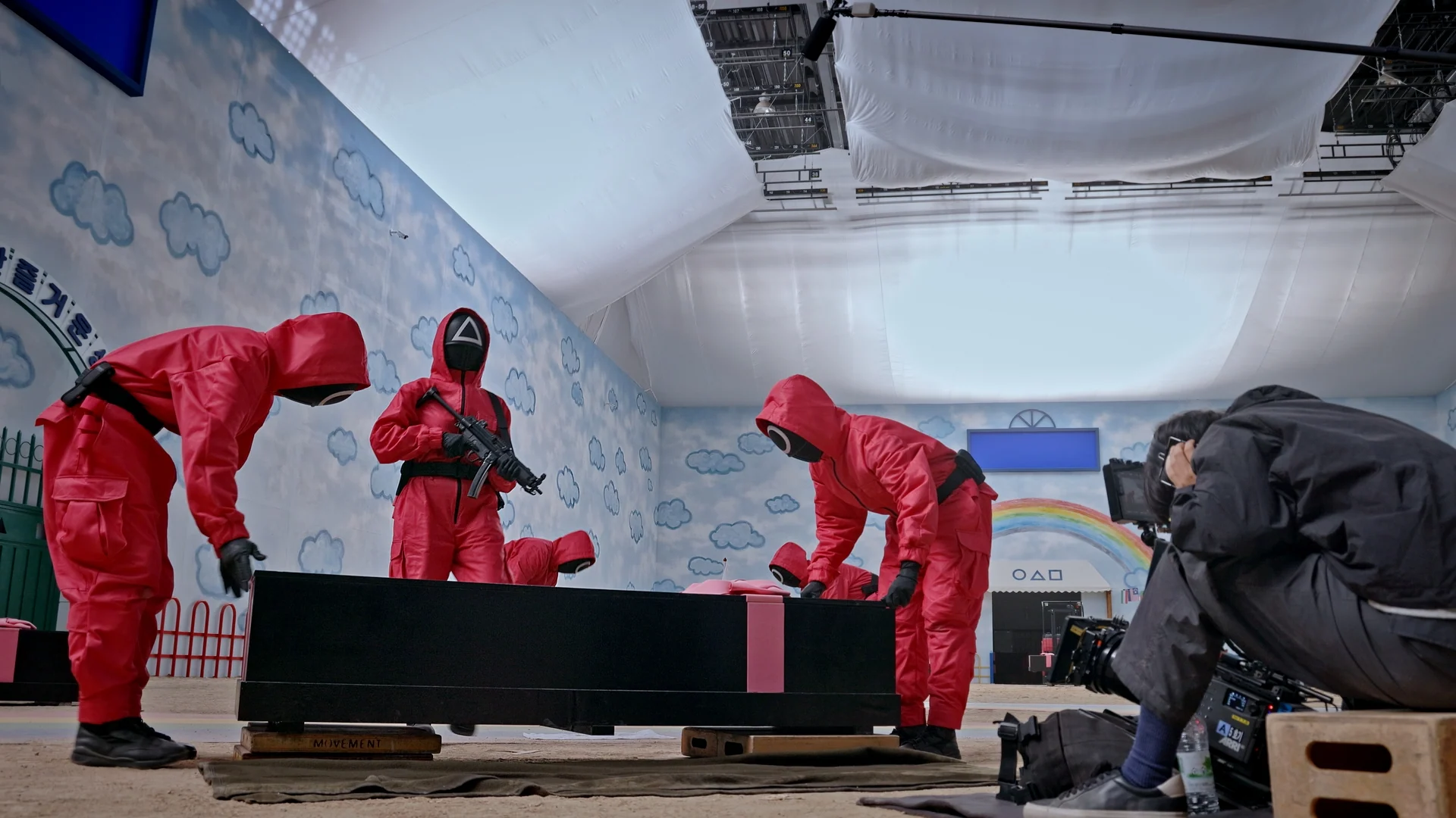 Inside Squid Game S2 — masked guards and crew staging the coffin on the nursery set