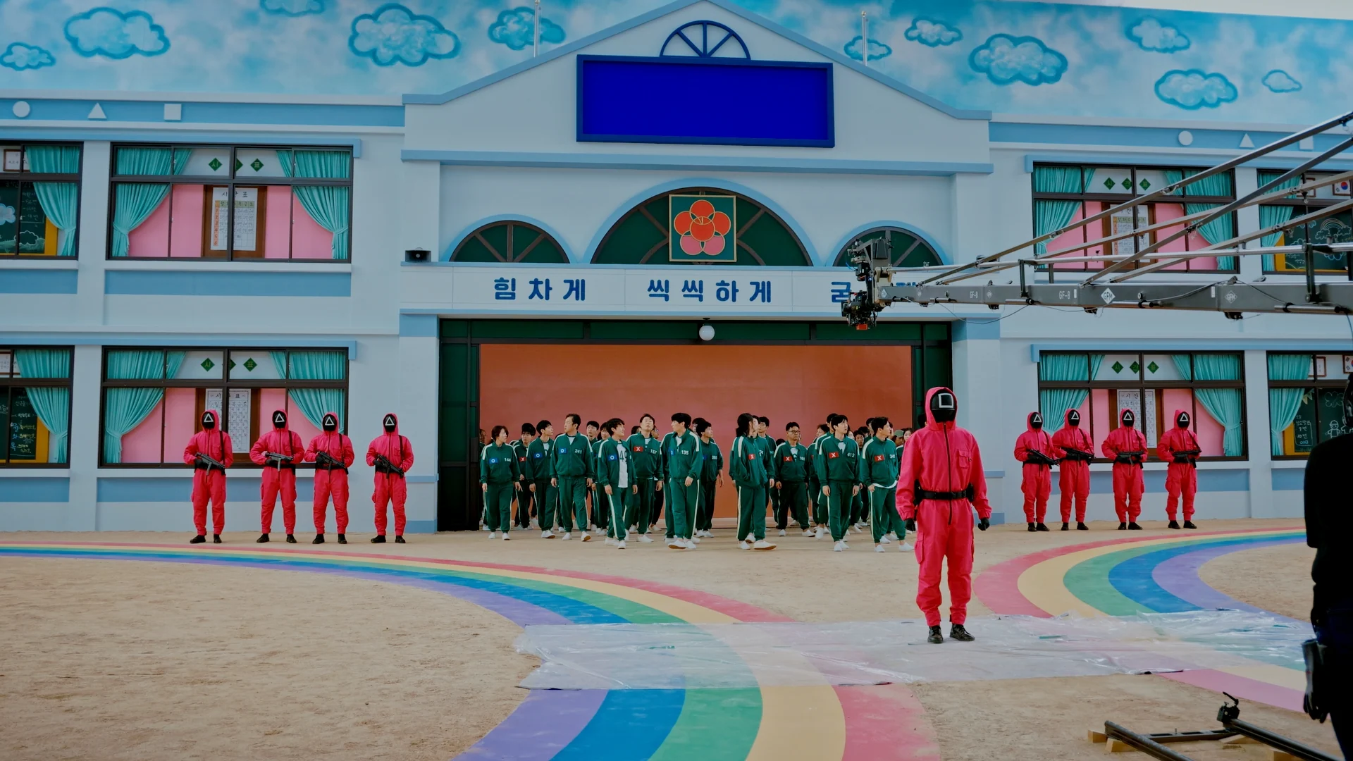 Inside Squid Game S2 — wide view of the rainbow staircase set with pink guards and film crew